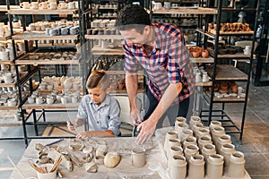 Attractive caucasian man and liitle cute boy kneading clay for pots.