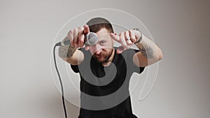 Attractive Caucasian man moves hands, microphone in hands, pointing to the camera grey background isolated medium shot