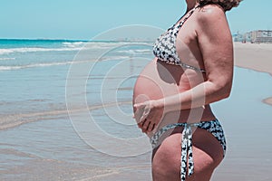 Attractive Caucasian pregnant woman posing against the sea holding her belly