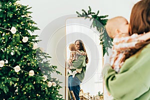 Attractive Caucasian redhead mother holding her baby and looking in the mirror on Christmas day.