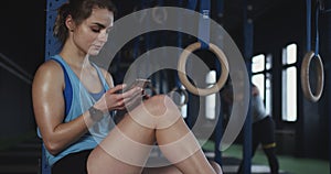 Attractive Caucasian sporty sweaty young woman using smart phone fitness tracker app after workout at modern gym.