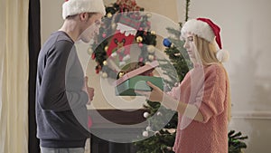 Attractive Caucasian woman in Christmas hat looking inside present, making displeased face, and giving gift back to man