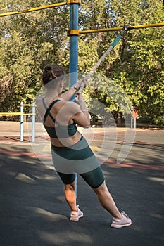 Attractive Caucasian woman doing pull-ups on a sports rope while exercising on a street sports ground.