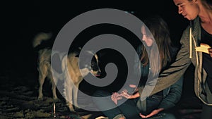 Attractive caucasian woman feeding cute dog sitting by the bonfire late at night. Closeup of kind woman`s hand with