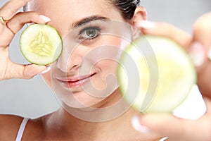 attractive caucasian woman holding and showing slices of cucumber