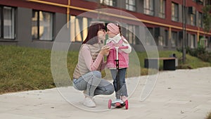 Attractive caucasian woman hugging her small girl, standing on scooter for child looking at each other