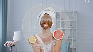 Attractive caucasian woman posing and having fun with half of lemon and grapefruit with brown mask on the face.
