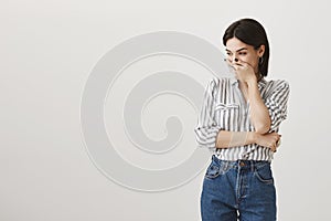 Attractive caucasian woman with short dark hair in stylish casual clothes mocking and chuckling, covering mouth, trying