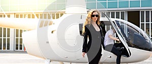 Attractive caucasion business woman with a helicopter and captain in the background. success and luxury concept