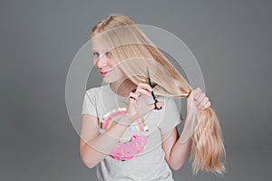 Attractive chaild girl is cutting her long blond natural hair