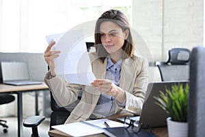 Attractive cheerful business woman checking paper documents in office, working on laptop