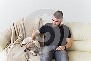 Attractive cheerful Caucasian male in casual t shirt sitting on couch favourite pet. Happy bearded man with his jack