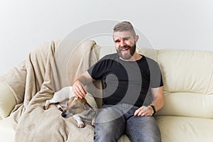 Attractive cheerful Caucasian male in casual t shirt sitting on couch favourite pet. Happy bearded man with his jack