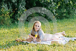 Attractive cheerful girl lying on a blanket and spending the weekend relaxing in the park outdoors