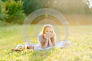 Attractive cheerful girl lying on a blanket and spending the weekend relaxing in the park outdoors