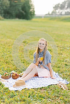 Attractive cheerful girl sitting on a blanket and spending the weekend relaxing in the park outdoors