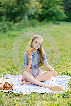 Attractive cheerful girl sitting on a blanket and spending the weekend relaxing in the park outdoors