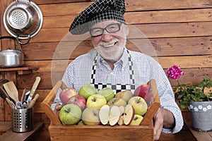 Attractive and cheerful senior man holds a basket full of apples of various qualities and colors. Rustic background in recycled