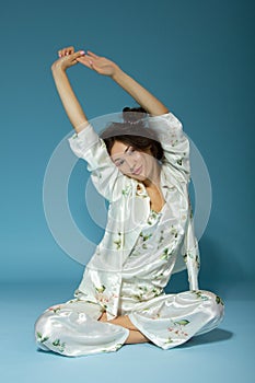 Attractive cheerful sleepy teen girl wearing pyjamas, isolated over blue background. Young pretty smiling woman in early before