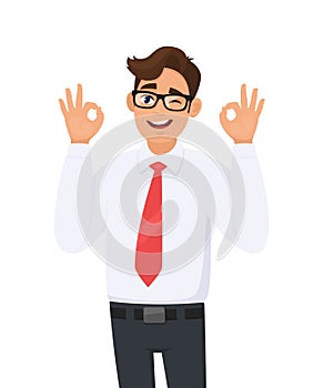 Attractive cheerful young business man showing/gesturing/making okay or ok sign, while winking eye. Human emotions, facial.