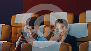 Attractive cheerful young caucasian couple using smartphone while watching film in movie theater. Lifestyle entertainment concept
