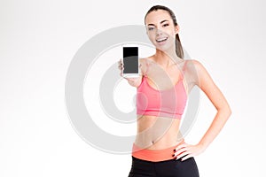Attractive cheerful young fitness woman showing blank smartphone screen