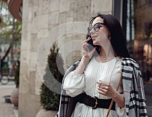 Attractive cheerful young woman in sunglasses speaking on cellphone in town street and smiling.