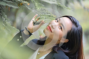 Attractive, Confidence young Asian Woman in business black suit is posting, smiling in front of leaves and tree with a relaxing