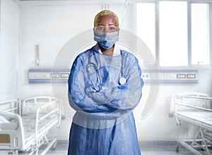 Attractive and confident black African American medicine doctor wearing face mask and blue scrubs standing corporate in health