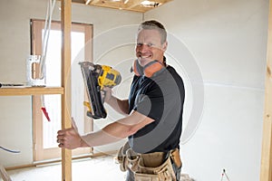 Attractive and confident constructor carpenter or builder man working wood with electric drill at industrial construction site