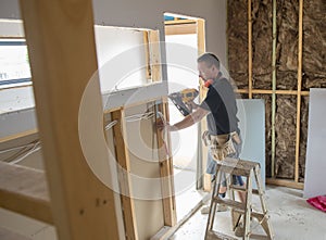 Attractive and confident constructor carpenter or builder man working wood with electric drill at industrial construction site