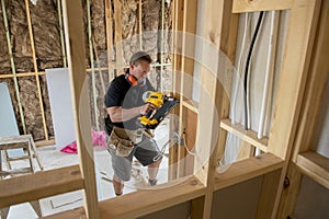 Attractive and confident constructor carpenter or builder man working wood with electric drill at industrial construction site photo