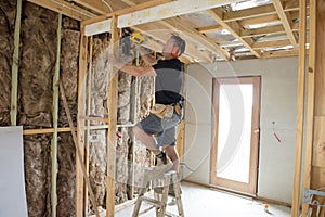 Attractive and confident constructor carpenter or builder man working wood with electric drill at industrial construction site photo