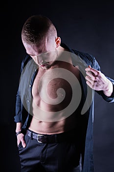 Attractive, Confident, young man with open shirt on muscular torso, ripped abs and pecs on black background.