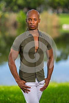 Attractive content young black man in thirties posing with thumbs in pockets at a park scene blurry background