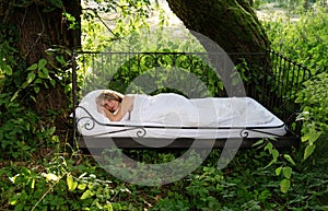 Attractive, content, young, sexy blonde woman lying in iron bed in the sun in nature
