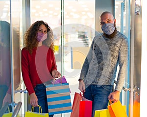Attractive couple of a bearded bolt man and a curly caucasian woman wearing face mask carrying paper bags inside the elevator at