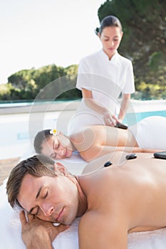 Attractive couple enjoying hot stone massage poolside