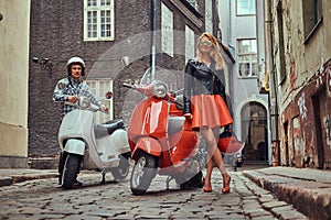 Attractive couple, a handsome man and female standing on an old street with two retro scooters.