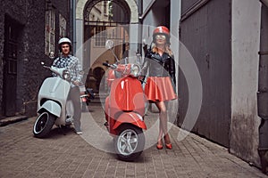 Attractive couple, a handsome man and female standing on an old street with two retro scooters.