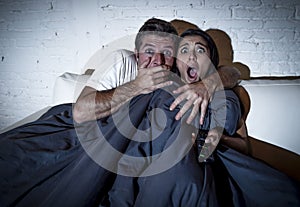 Attractive couple at home enjoying watching television horror movie covering with blanket