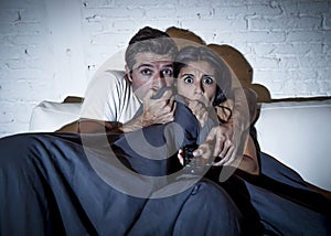 Attractive couple at home enjoying watching television horror movie covering with blanket