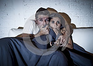 Attractive couple at home enjoying watching television horror movie covering with blanket photo