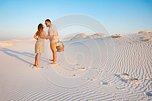 Attractive couple kissing on the white sand beach or in the desert or in the sand dunes, guy and a girl with a basket in their han