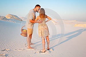 attractive couple kissing on the white sand beach or in the desert or in the sand dunes, guy and a girl with a basket in their ha