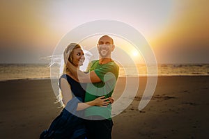Attractive couple in love hugs and laughs on the beach at sunset. Happy people rest on the sea. Bright backlight from sun