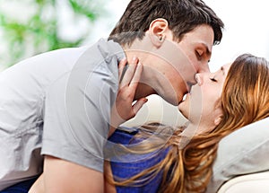 Attractive couple of lovers kissing itself lovingly on a sofa