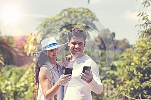 Attractive Couple Messaging Online Using Smart Phones Man And Woman Embracing Over Tropical Forest Landscape Smiling