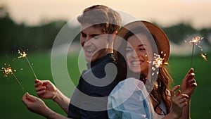 Attractive couple moving with lights in park. Guy and girl posing with sparklers