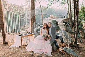 Attractive couple newlyweds, happy and joyful moment. Man and woman in festive clothes sit on the stones near the